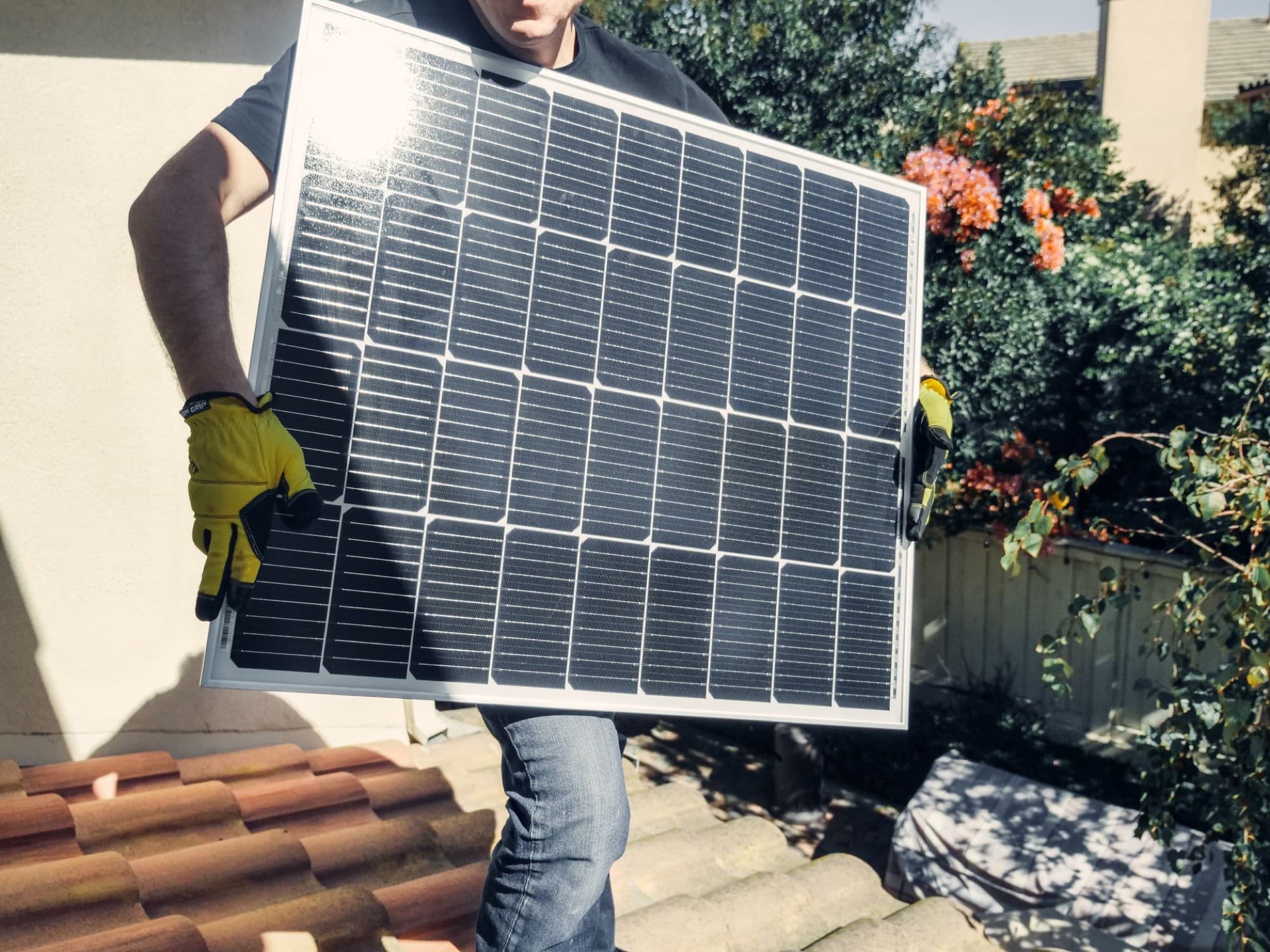 A worker carrying a solar module onto a tiled house roof