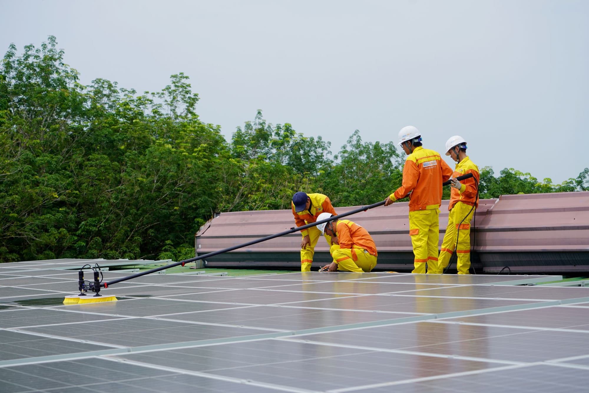 A crew cleaning a rooftop array with a soft brush on a long pole