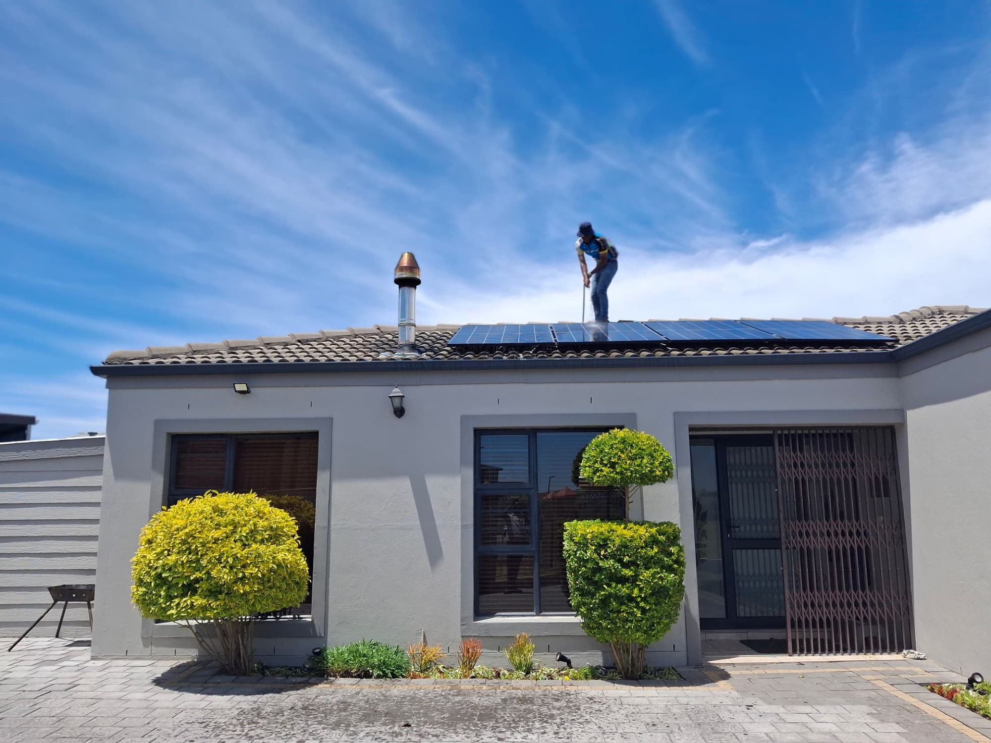 A technician on the roof of a house, panels going up under a clear sky